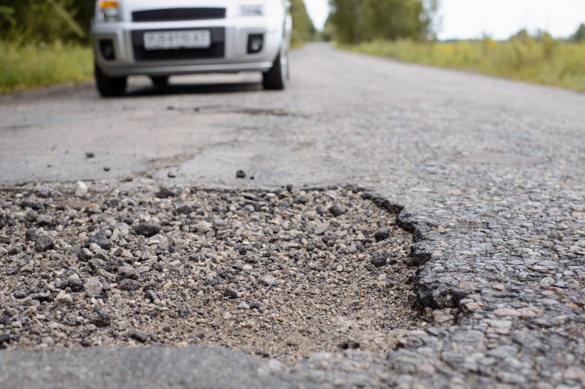 pothole in road with car in the background